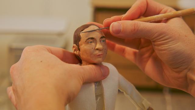 hands hold a claymation puppet and use a tool to smooth out the forehead of the character