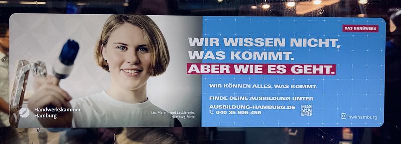 Anzeige der Handwerkskammer Hamburg. Strenges Querformat in S-Bahn. In der linken Hälfte eine junge blonde, kurzhaarige Frau (Bobfrisur?), die in der Frontalansicht zum Betrachter einen dunkelblau gefärbten Rundpinsel  in ihrer rechten Hand hält. 
Rechts ein in den Farben der Handwerkskammer Hamburg gehaltenem Blau steht weiß auf blau: WIR WISSEN NICHT, WAS KOMMT.
ABER WIE ES GEHT (weiß auf rot).
WIR KÖNNEN ALLES, WAS KOMMT.
FINDE DEINE AUSBILDUNG UNTER

Darunter Adresse und Telefonnummer, um sich zu einem passenden Beruf zu melden.