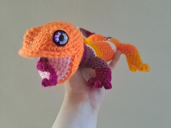 Salamandre au crochet, bouche ouverte : alternances de bandes orange foncé, orange clair, blanc, violet clair, violet.  Une langue bifide sort de sa bouche