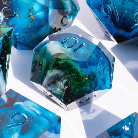 A D12 surrounded by other TTRPG dice. The dice are translucent light blue with swirls of white and green and have reflective bronze specks in them.