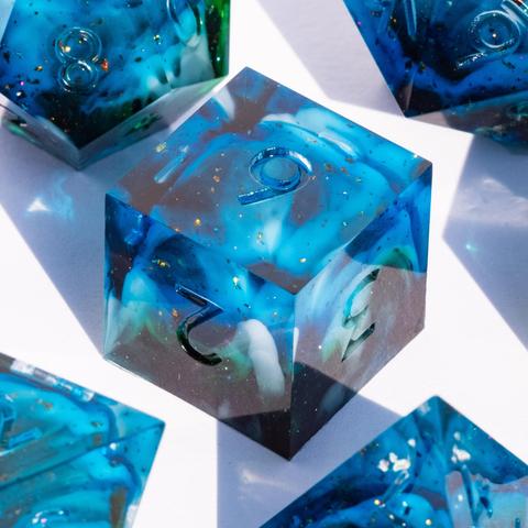A D6 surrounded by other TTRPG dice. The dice are translucent light blue with swirls of white and green and have reflective bronze specks in them.