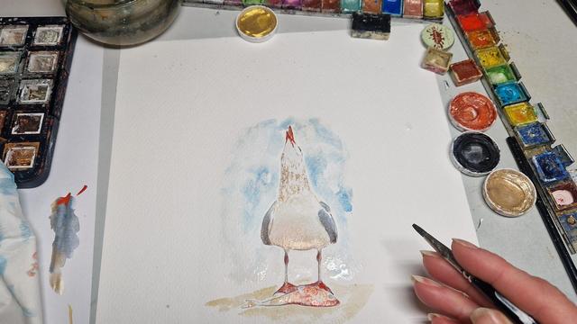 Male eine Möwe die vor einem auf dem Boden liegenden Fisch steht und triumphierend den Kopf nach oben streckt