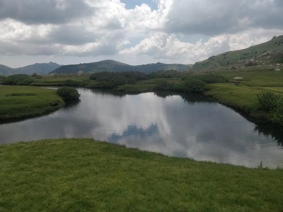 Photo d'une rivière entourée d'herbe, pozzis en corse, le ciel nuageux se reflète dans l'eau