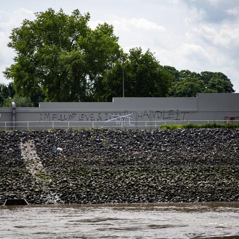 Eine Mauer am Ufer der Elbe. Sie ist in schwarzer Farbe besprüht mit dem Spruch "I'm full of love & I can't handle it". Das "can't" ist in weißer Farbe durchgestrichen und es ist "will" darüber gesprüht.