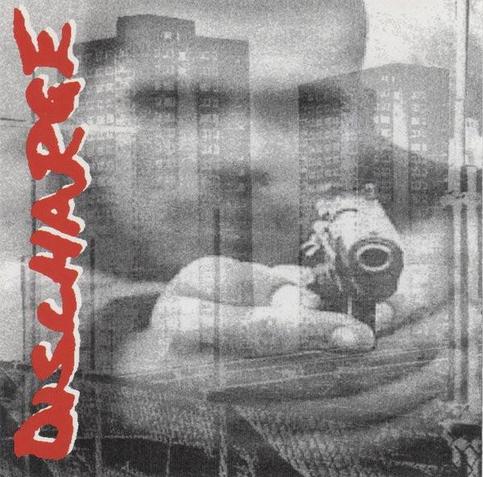 Superposition en noir & blanc de deux immeubles de banlieue derrière un grillage et d'un homme qui braque son revolver dans notre direction. Le nom du groupe Discharge (avec sa police habituelle) est en rouge à la verticale et à gauche