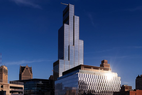 A modern skyscraper with a reflective glass facade stands tall against a deep blue sky in an urban skyline.