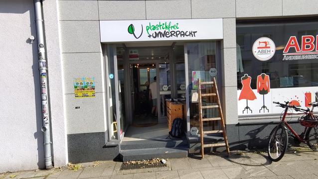 Außenansicht eines Ladens mit weißer Leuchtreklame über dem Eingang auf der steht in grün und schwarz: plastikfrei + unverpackt.