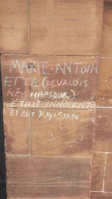 Chalked graffiti on a red, stone wall, written in French, basically proclaiming Marie Antoinette to have been innocent and correct