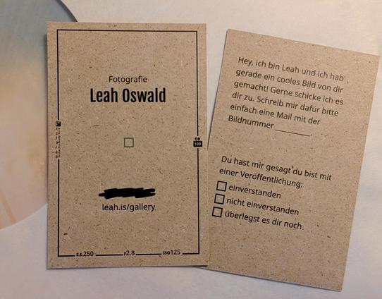 Zwei Visitenkarten nebeneinander. Einmal die Vorderseite und einmal die Rückseite. Auf der Vorderseite steht Fotografie und dann größer Leah Oswald. Darunter ein kleiner grüner Kasten in der Mitte der Karte der den scharf gestellten Autofokus symbolisiert. Im schwarzen Rahmen der Karte sind einige Werte wie S.S 250, F2.8 oder ISO 125 hinterlegt. Auf der Rückseite steht: Hey, ich bin Keah und hab gerade ein cooles Bild von dir gemacht! Gerne schicke ich es dir zu. Schreib mir dafür bitte einfach eine Mail mit der Bildnummer ____. Außerdem etwas weiter unten: Du hast mir gesagt, du bist mit einer Veröffentlichung und dann eine Auswahl zwischen "einverstanden", "nicht einverstanden" und "überlegst es dir noch"