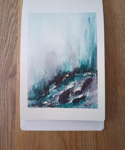 This is an Atmospheric Watercolor Landscape Painting in portrait orientation in an A5 sketchbook using DS Moonglow and Ultramarine Turquoise. Along the curving horizon line are masstones of both colors that are them pushed with water above the horizon line where they bloom to medium values and then disperse upward creating the atmospheric affect. Grasses and added texture start at the horizon line and mark the terrain with dark, medium, and light values and granulation.