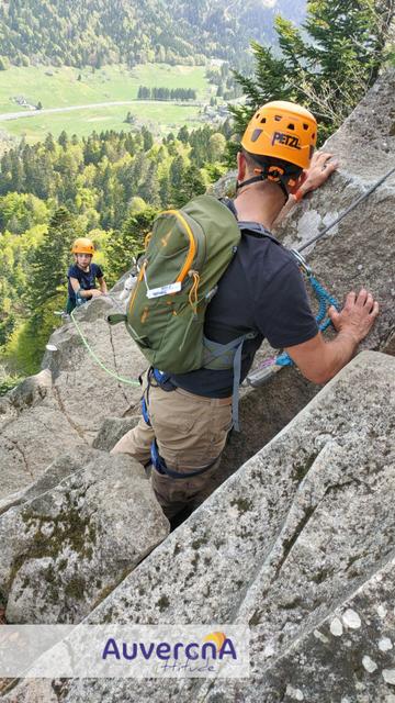 Enfant et son papa engagés sur la via-ferrata du Capucin (Mont-Dore), avec vue sur le fond de vallée.