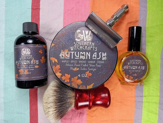 (Le Chat Mistral description)

The image showcases a collection of grooming products from Southern Witchcrafts, arranged on a striped background. There is a dark bottle of Autumn Ash aftershave splash, a round tin of shaving soap with autumn leaf designs, and a small bottle of eau de parfum. Additionally, there is a shaving brush with a red handle and a safety razor. The products are labelled with "Southern Witchcrafts" and have a consistent autumnal theme, featuring scents like maple, spice, smoke, amber, and cedar. The arrangement is neat and visually appealing, with the items placed closely together.