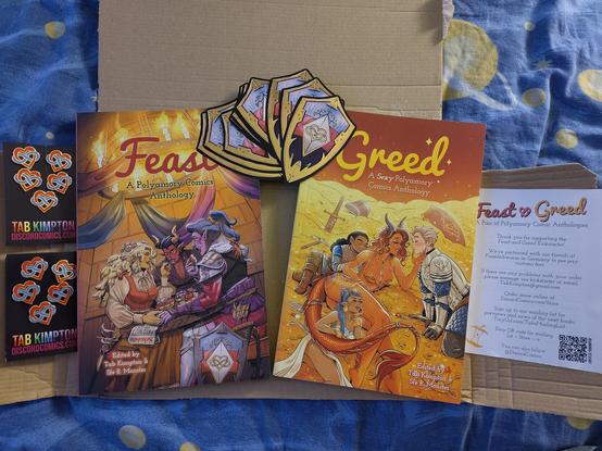 A wellpapp box is opened up. The books Feast and Greed with colorful artwork is in the middle.
Their cover pages are very fantasy inspired with Feast having the setting of a tavern where what likely is a human, a demon and an orc sharing a meal and schedule. The front page of Greed is in a treasure chamber, a humanoid dragon is seducing two knight, a human and an elf. And by the dragon's tail is another elf looking comfy dreamy. 
Across the top of books are stickers shaped like a shield, stripes of blue, pink and purple. Golden trim around it's edge and a golden heart with the infinity sign across in the center of the shield. 
Next to the books are pins of hearts with the infinity sign across and a note about the books.