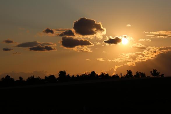 Abendsonne mit ein paar dunkle Wolken am orange erhellten Abendhimmel. Im Vordergrund sieht man die Silhouette eines Waldes.
Matzework