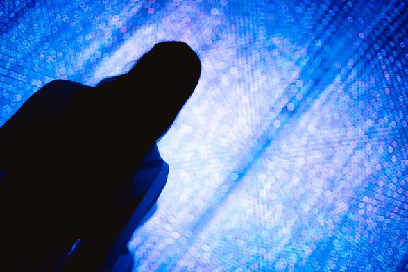 photo of the solhouette of a person standing in front of a wall of blue lights, which itself appear blurred by bokeh