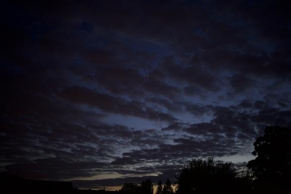 Der mit dünnen, niedrigen Wolken teilweise bedeckte Nachthimmel 2 Tage nach der Sommersonnenwende.
Am Horizont zeichnen sich Dächer und Bäume gegen den orangenen durch die nur knapp unter dem Horizont stehende Sonne erleuchteten Himmel ab.
(f2, 1/25 s, iso 1600)