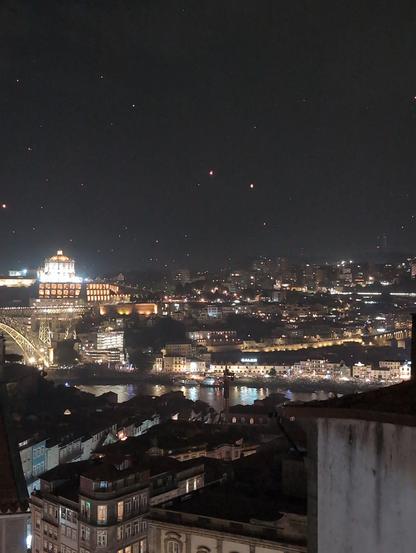 Rio Douro na noite de São João com edifícios ilumunidas e muitos balões de papel no ceu