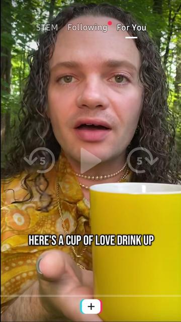 Guy with long curly hair in yellow shirt saying "Here's a cup of love, drink up!"