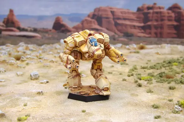 A painted miniature of a Supernova 'Mech.  It is painted in tan and brown desert camo.  The black scorpion emblem of Clan Goliath Scorpion is on the left torso, and the Mu Galaxy emblem, the letter "M" on a sun, is high on the right torso.  The miniature is photographed on desert terrain.