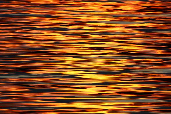 Photo of bright yellow and orange sunset light reflected on ripples in a lake.