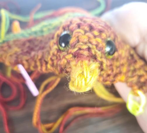 A partially constructed knitted chickie with green safety eyes installed