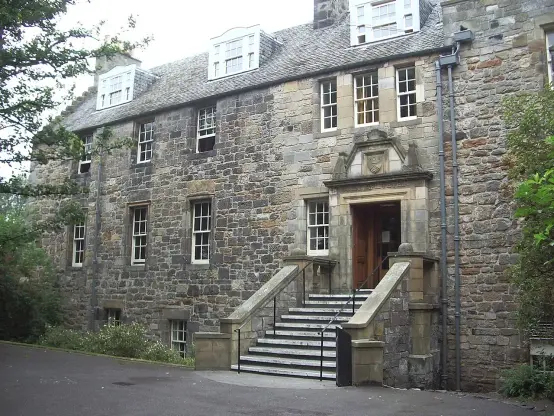 The image shows a historical building made of stone. It features a set of stairs leading up to a grand entrance that includes a wooden door. There are multiple windows above and beside the entrance. The building has a classic architectural style, with a sloped roof and decorative elements around the doorway. Surrounding the structure are trees and greenery, adding to the picturesque setting.

Image Credits: Wikimedia / Irlmex / CC BY-SA 3.0