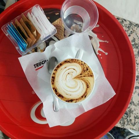 A cup of cappuccino on a red tray with sugar packets and a glass of water.