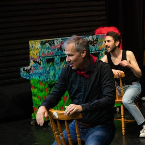 Deux membres du cast à califourchon sur des chaises en bois pour la chanson hot du show.
