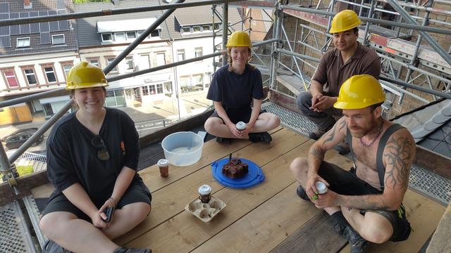 Baustellenplanung auf der fünften Gerüstlage...
Nee, war ein Scherz. Unser Geselle ist gestern zu spät gekommen, hat dafür aber Kaffee mitgebracht, um es wieder gut zu machen - was super gepasst hat, weil die Praktikantin ihren "Einstandskuchen" dabei hatte. 
deshalb gab es Picknick auf der 5. Gerüstlage. so hatten wir alle was davon.
das Foto zeigt die Praktikantin (hinten mit Becher), den Helfer (vorne rechts, mit Kaffee) und zwei Gesell*innen aus dem Formenpark mit den Resten von Kaffee und Kuchen.
