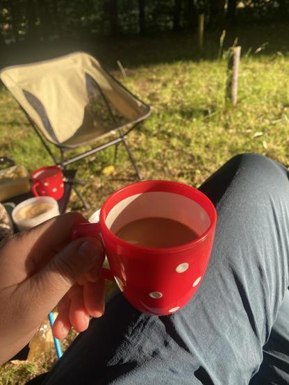 Der Kaffee in einer rot-weiß gepunkteten Tasse in der Hand, sitzend in der Morgensonne