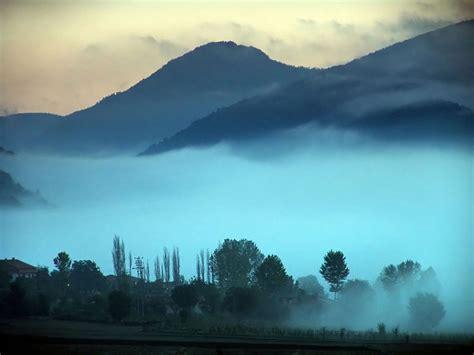 Image shows silhouetted hills with the sun low in the sky. The valley is hidden by thick mist.