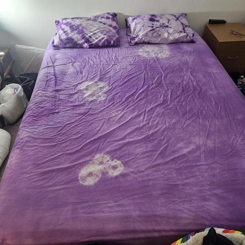 the fitted sheet with pillows on top: the pillows are pale purple and dark purple in abstract patterns, while the fitted sheet is a medium purple with a few clusters of pale purple circles