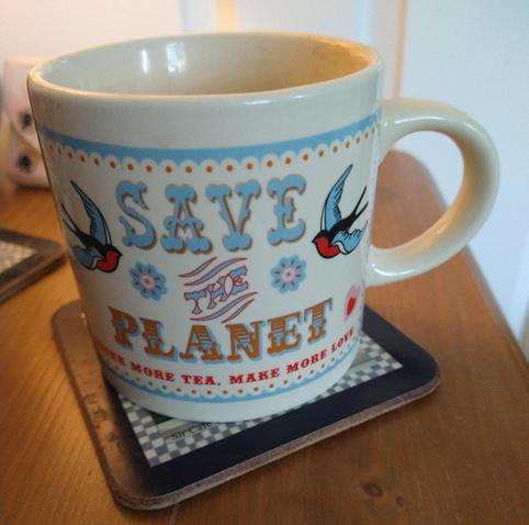 Mug of tea on a bedside cabinet, it has bluebirds on either side, and the words save the planet in the middle