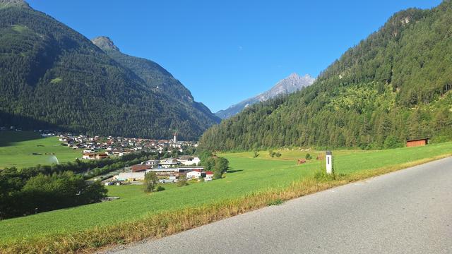 Kitsch alpine landscape with rocks, meadows, forests, village, church, blue sky.