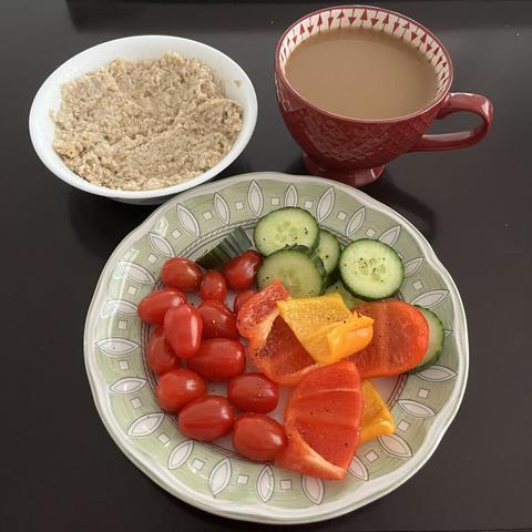 A plate of sliced peppers and cucumbers and cherry tomatoes seasoned with salt and pepper, a small bowl of oatmeal with brown sugar mixed in, and a cup of almond coffee.