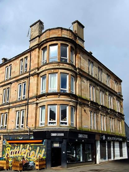A blonde sandstone corner tenement with a mural saying Battlefield on the side of one of its ground floor commercial spaces.