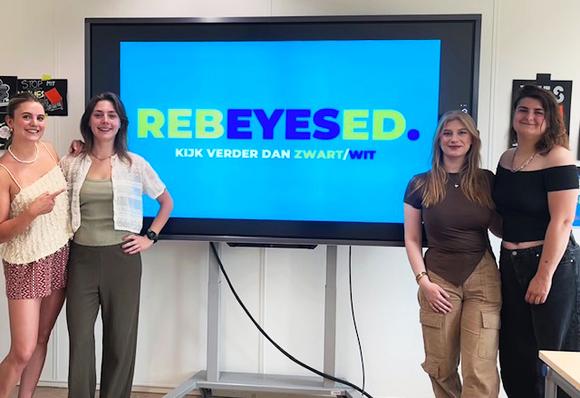 Communicatiestudenten zetten zich in tegen mediabias met platform RebEYESed. OP deze foto staan ze met z'n vieren bij een beeldscherm met het logo