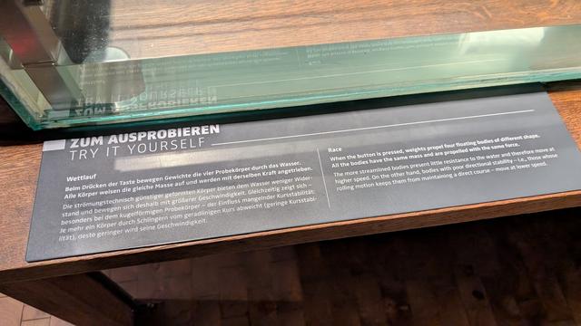Experimentieranordnung für Strömungen. Vier Formen mit unterschiedlicher Gestalt in einem Wasserbecken. Gewichte ziehen an ihnen.
