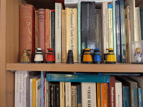 two trios of lego daleks with their black overlord, and me in a glass box, knitting of course. sitting on a book case