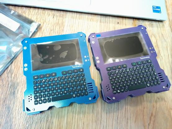 Two squarish, cyberdeck like devices with a screen and a keyboard. One is blue, the other purple
