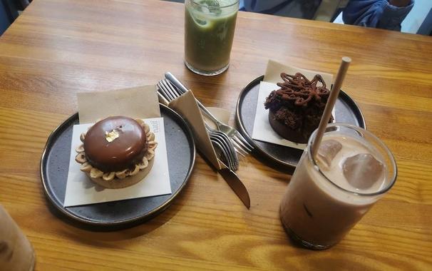 An overhead shot reveals two decadent desserts, a green drink, and a chocolate iced drink on a wooden table.