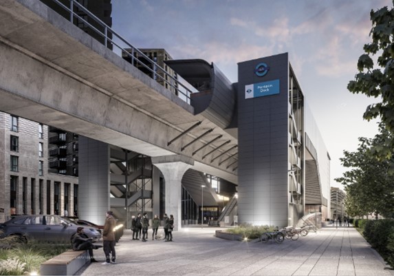 A modern transport station entrance featuring a large, grey structure with a sign indicating "Pudding Dock." The station is elevated above ground level, supported by concrete pillars, with a wide pathway leading to the entrance. A group of people is gathered outside, and a few bicycles are parked nearby.

TfL Graphic - Artist's Impression of Pontoon Dock 1
