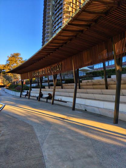 A seating area near Parramatta Quay. It's a fairly new and highly varnished wooden structure that looks a bit like a stadium grandstand. Underneath are several rows of concrete bleachers.