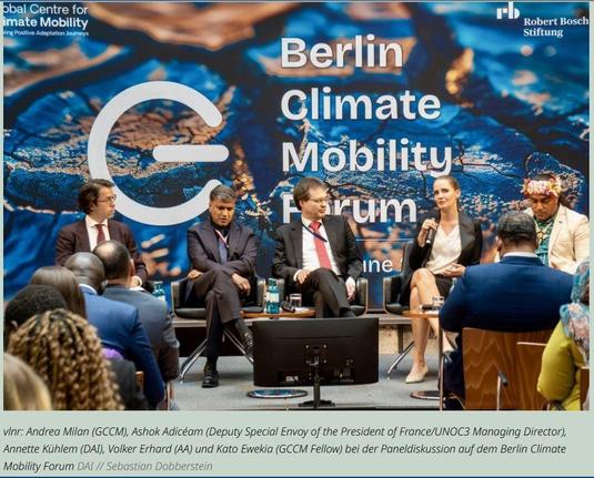 Fünf Personen sitzen auf einer Bühne in einer Podiumsdiskussion beim Berlin Climate Mobility Forum. Im Hintergrund ein großes Banner mit dem Schriftzug des Forums. Eine Frau spricht mit einem Mikrofon, ein Mann rechts von ihr trägt einen traditionellen Kopfschmuck. Im Vordergrund sieht man das Publikum. Bildunterschrift: vlnr: Andrea Milan (GCCM), Ashok Adicéam (Deputy Special Envoy of the President of France/UNOC3 Managing Director), Annette Kühlem (DAI), Volker Erhard (AA) und Kato Ewekia (GCCM Fellow) bei der Paneldiskussion auf dem Berlin Climate Mobility Forum.