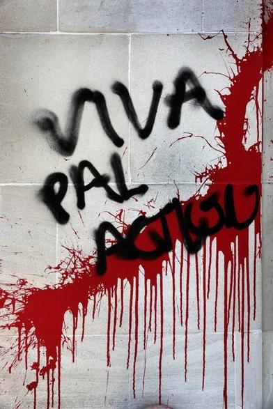 Close up of part of the wall of a building with red paint splattered on it, together with the words VIVA PAL ACTION in black capitals.