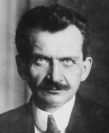 Eine Schwarzweißfotografie von einem etwa mittelalten Mann mit dunklem Haar, dichtem Schnurrbart und ausgeprägten Geheimratsecken. Er trägt Anzug und Krawatte, seine hellen Augen blicken direkt in die Kamera. Es handelt sich um Otto Wels.