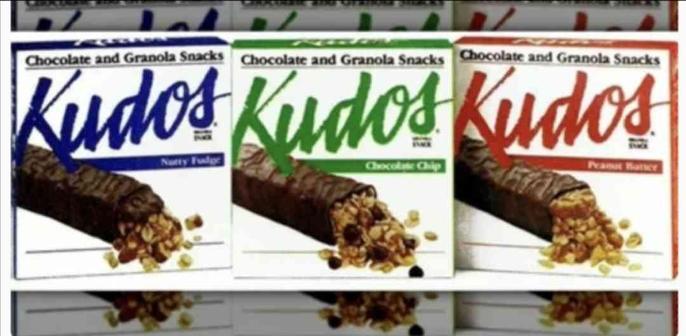 The image displays three boxes of "Kudos" brand chocolate and granola snacks, lined up horizontally, each representing a different flavor.