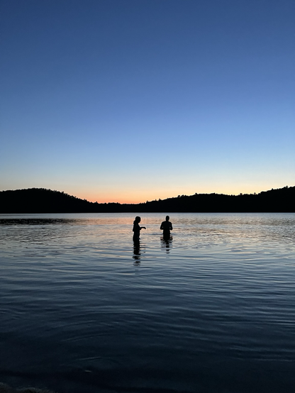 Two people in a lake against the sunset.
