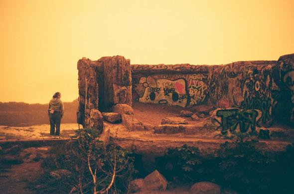 A woman standing next to the ruins of the Sutro Baths, the crumbling concrete walls tagged with different graffiti.