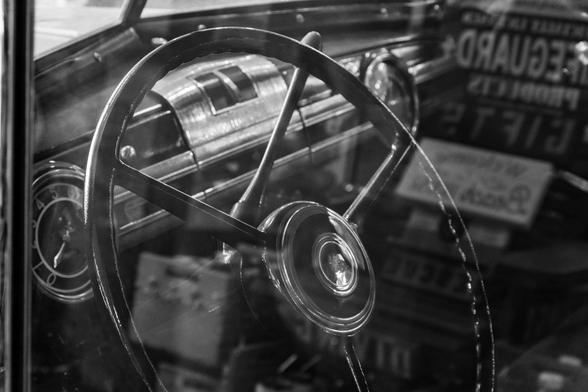 The inside steering wheel and dash of a restored 1939 Packard as shot through the drivers side window.  The window is very reflective and mingles the inside of the car with the outside.